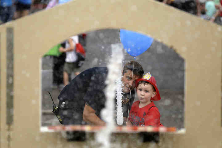 Lt. Kevin Childs, with Truro Township Fire Department, helps Joseph Finnerty II, 5, of Reynoldsburg, spray some targets at a firefighter game during the fourth annual National Night Out event, hosted by the Reynoldsburg Division of Police.  (Shane Flanigan / ThisWeek Community News)